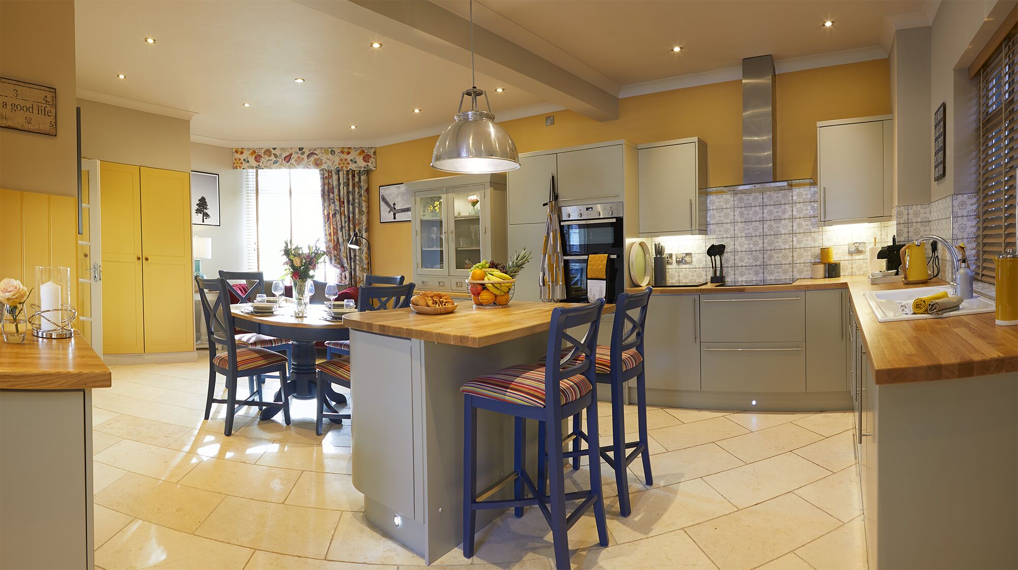 A modern kitchen with a central island, dining area, and a large window.