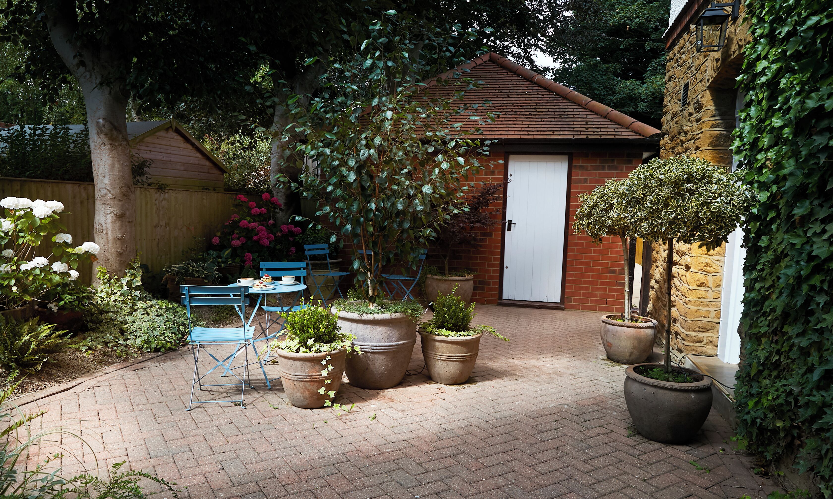 A brick patio with potted plants and blue chairs.
