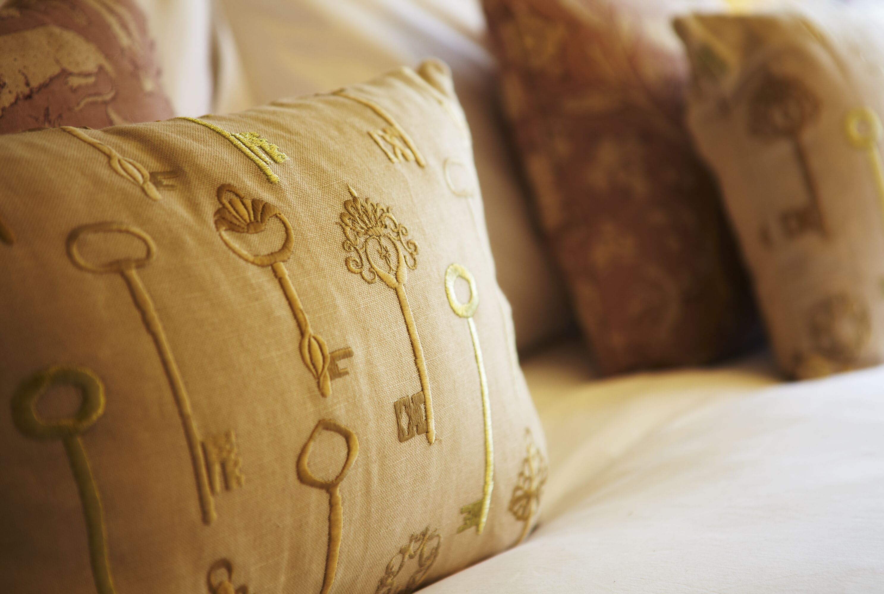 A close-up of a bed with a beige pillow featuring embroidered keys and a tree design.