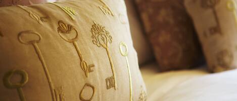 A close-up of a bed with a beige pillow featuring embroidered keys and a tree design.