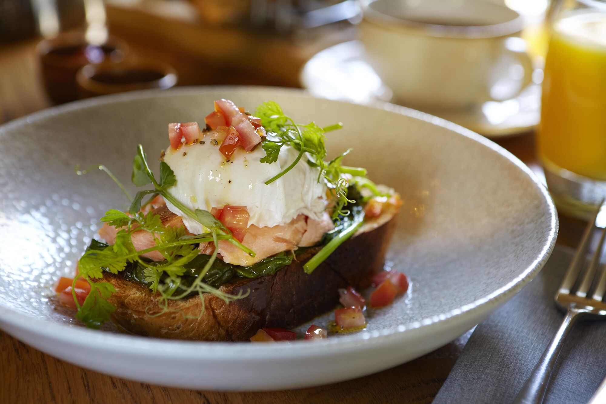 A plate with a poached egg, greens, and diced tomatoes on a textured white plate.