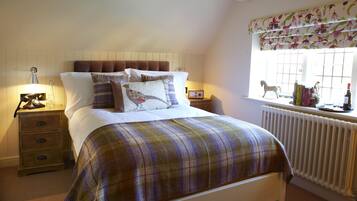 A neatly made bed with a plaid bedspread, a bedside table with a lamp, and a window with a floral valance.