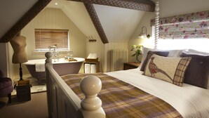 A bedroom with a large bed, a window with floral curtains, a built-in bathtub, and a wooden ceiling. - The Plough Scalby (Scarborough)