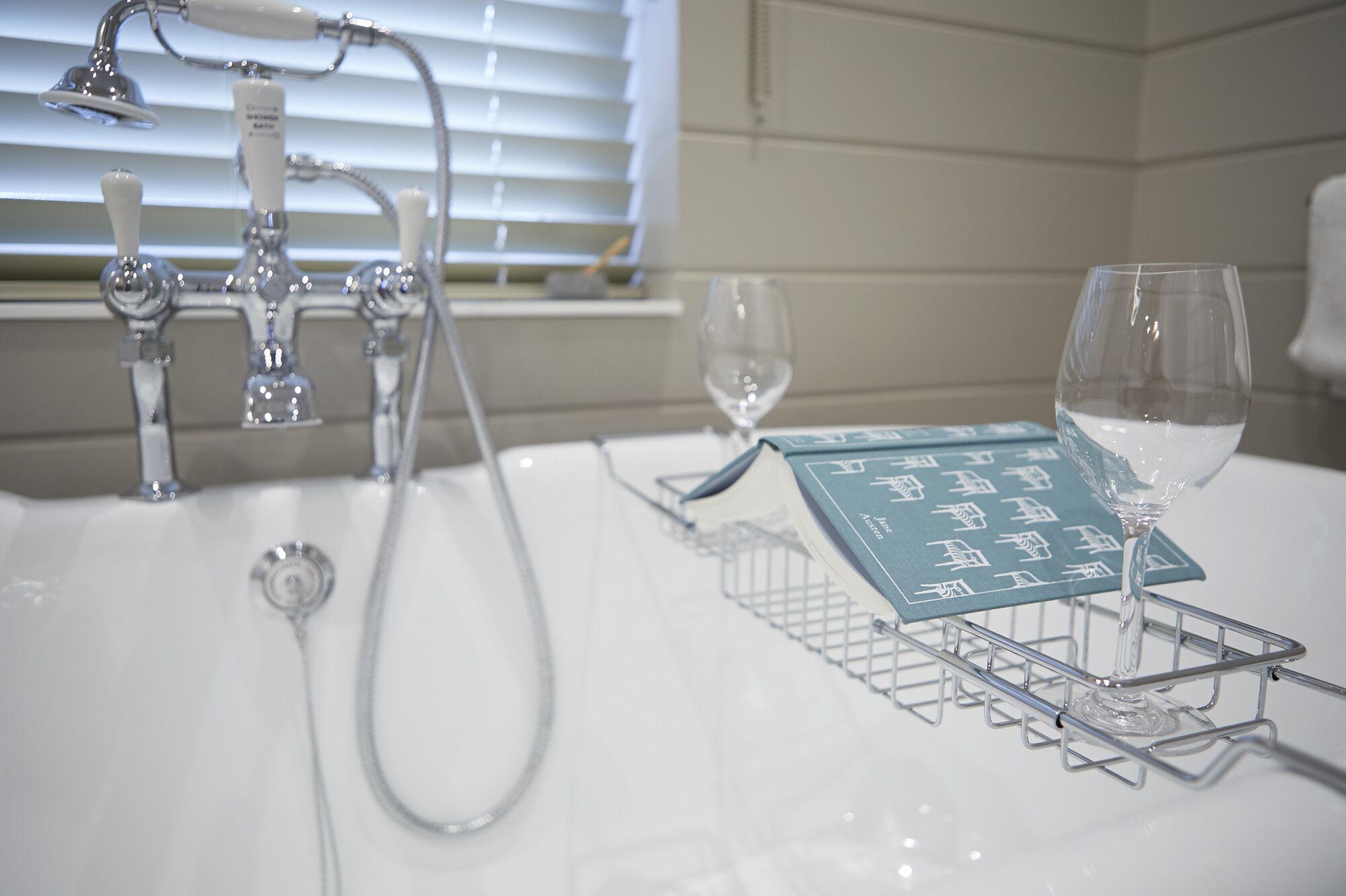 A bathroom with a white sink, a handheld showerhead, and a glass wine glass on a wire rack.