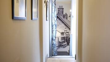 Um corredor com quadros nas paredes, uma cortina estampada e vista para a rua com um banco e um edifício.