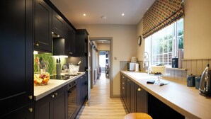 A modern kitchen with dark cabinetry, a wooden countertop, and a window with a patterned valance. - The Plough Scalby (Scarborough)