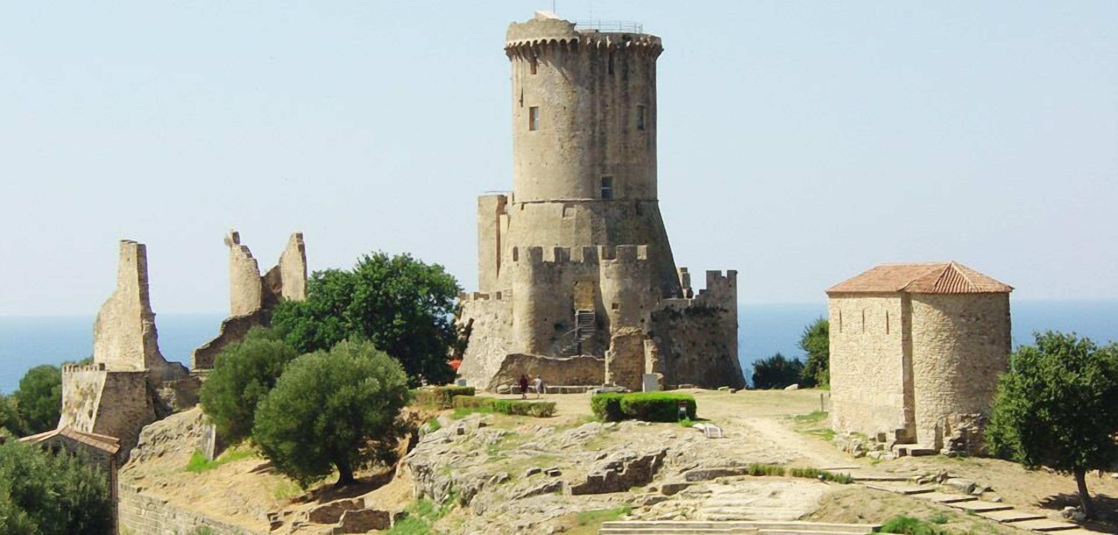 Eine historische Steinburg mit einem markanten Turm, Ruinen und einem kleinen Gebäude.