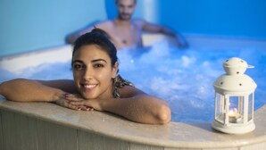 Uma pessoa relaxando em uma banheira de hidromassagem com um candeeiro, e outra pessoa ao fundo.