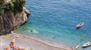 A beach with clear blue water, a rocky cliff, and several boats. - Rumi Hotels & SPA (Ascea)