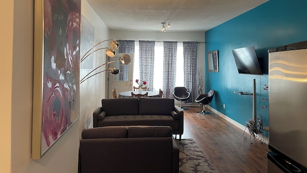 A modern living room with a sofa, a dining table with chairs, a TV mounted on the wall, and a ceiling fan. - Barefoot Inn (Ottawa)
