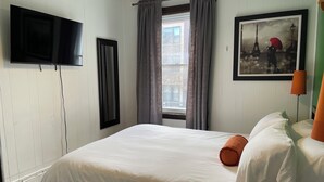 A hotel room with a bed, a TV mounted on the wall, a window with curtains, and a framed picture on the wall. - Barefoot Inn (Ottawa)