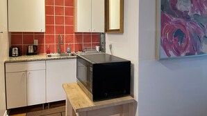 A compact kitchen with white cabinets, a red tiled backsplash, a microwave on a wooden stand, and a large abstract painting on the wall. - Barefoot Inn (Ottawa)