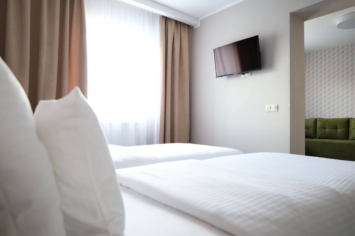Une chambre d’hôtel avec deux lits, un téléviseur à écran plat fixé au mur et une tête de lit recouverte d’un tissu vert.