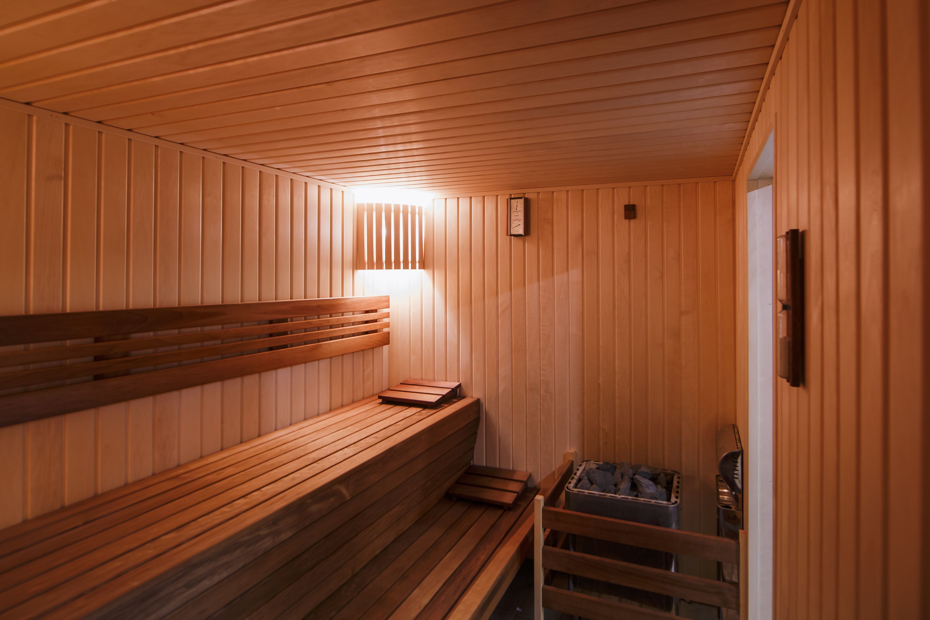 Una sauna con bancos de madera, un asiento tipo banco y un calentador.