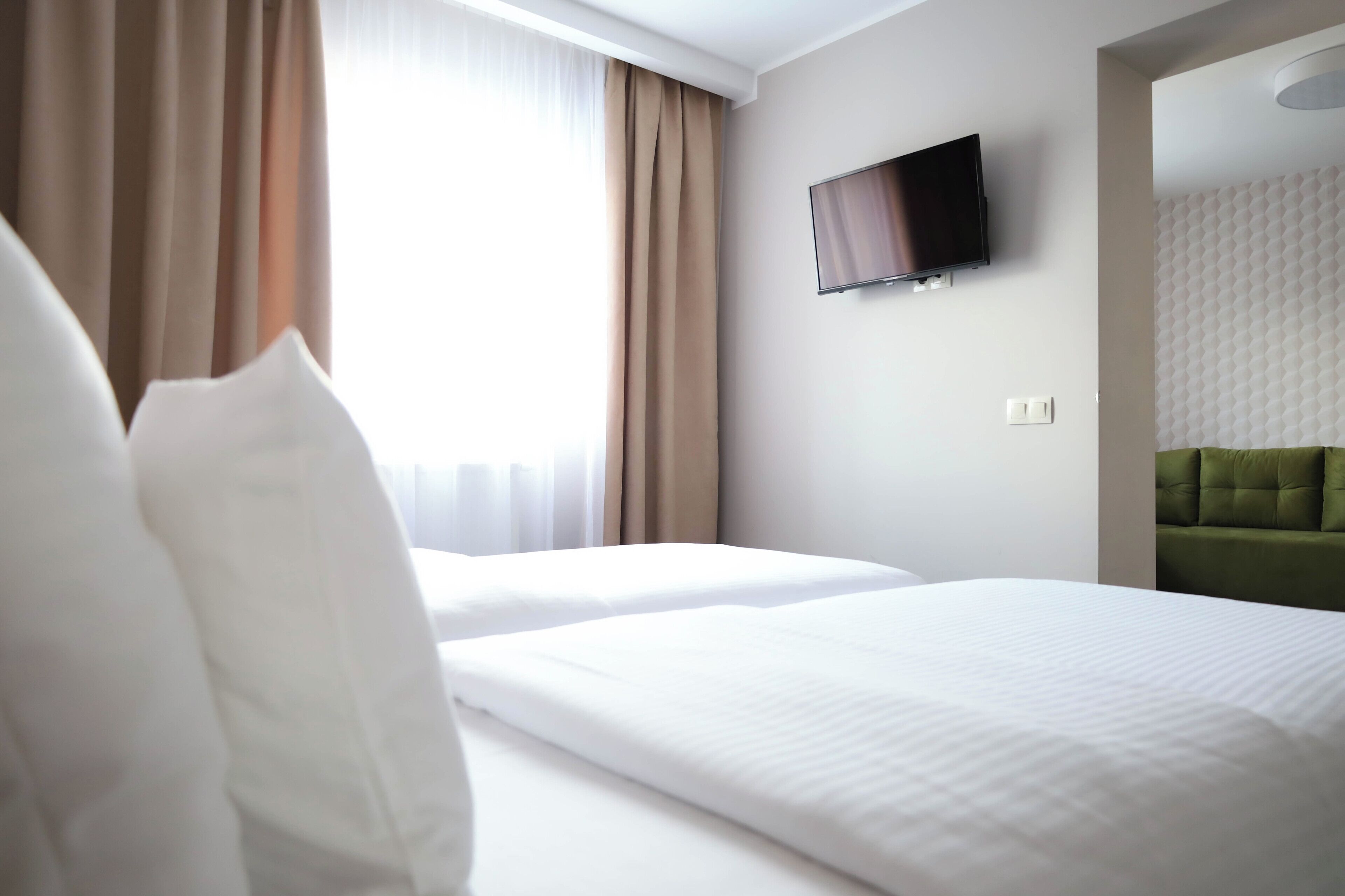 A hotel room with two beds, a flat-screen TV mounted on the wall, and a green upholstered headboard.