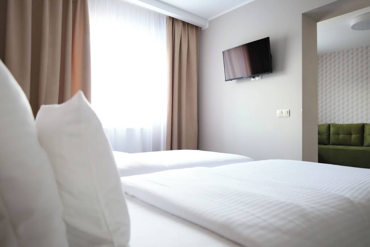 Une chambre d’hôtel avec deux lits, un téléviseur à écran plat fixé au mur et une tête de lit recouverte d’un tissu vert.