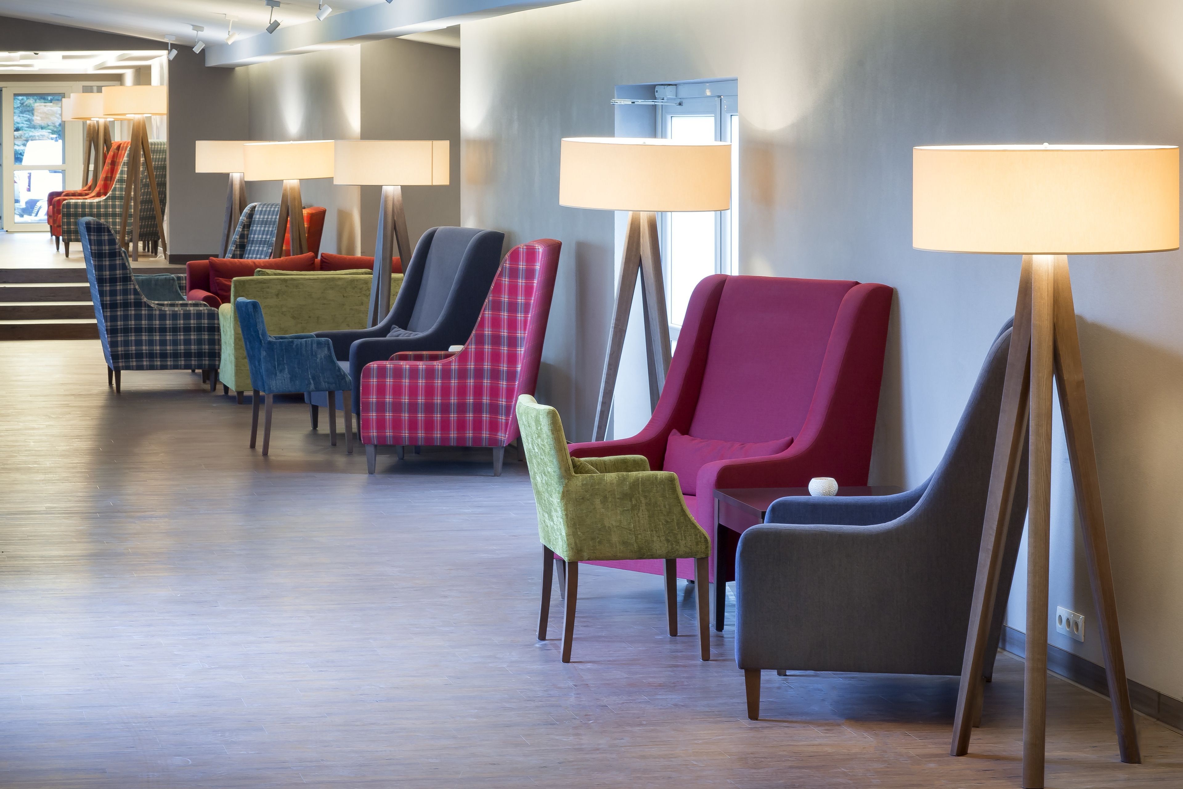 Un hall de hotel con una fila de sillones coloridos y lámparas de pie.