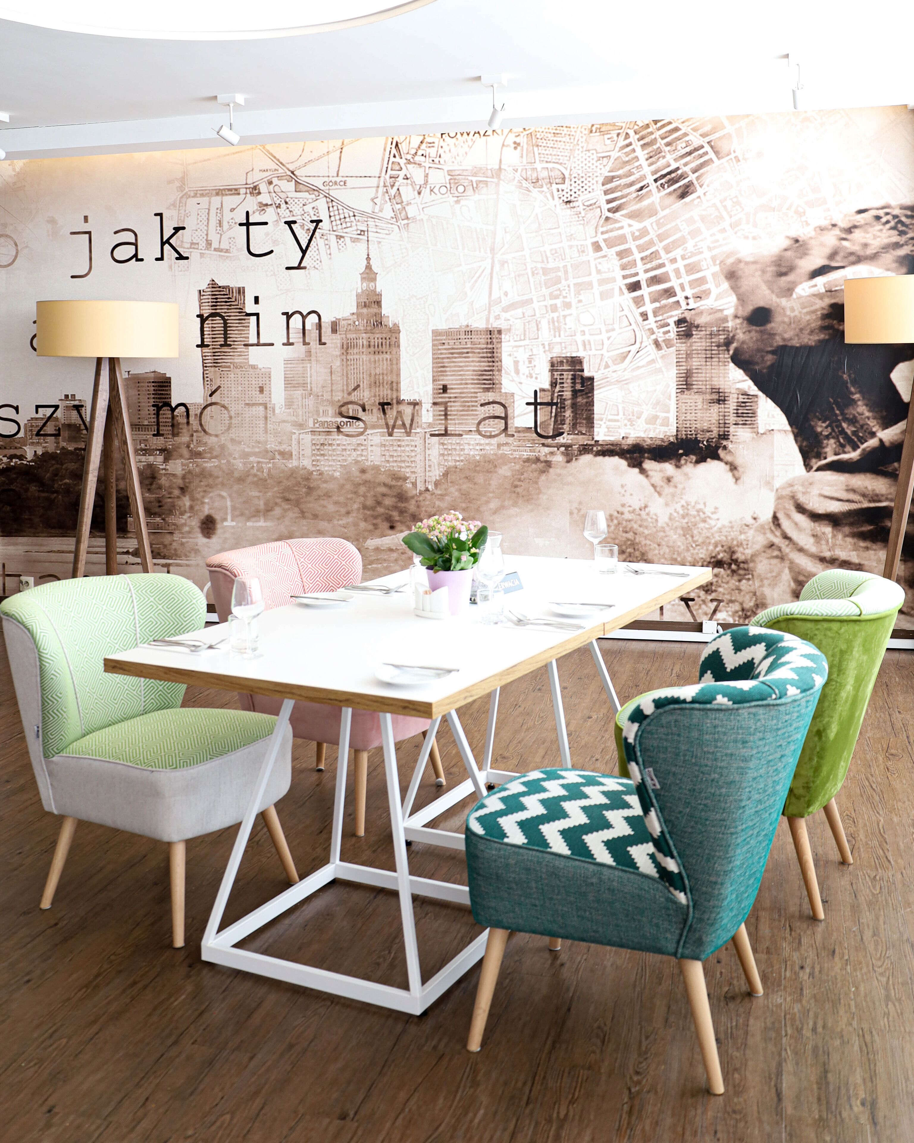 A dining area with a white table, green and teal chairs, and a cityscape mural in the background.