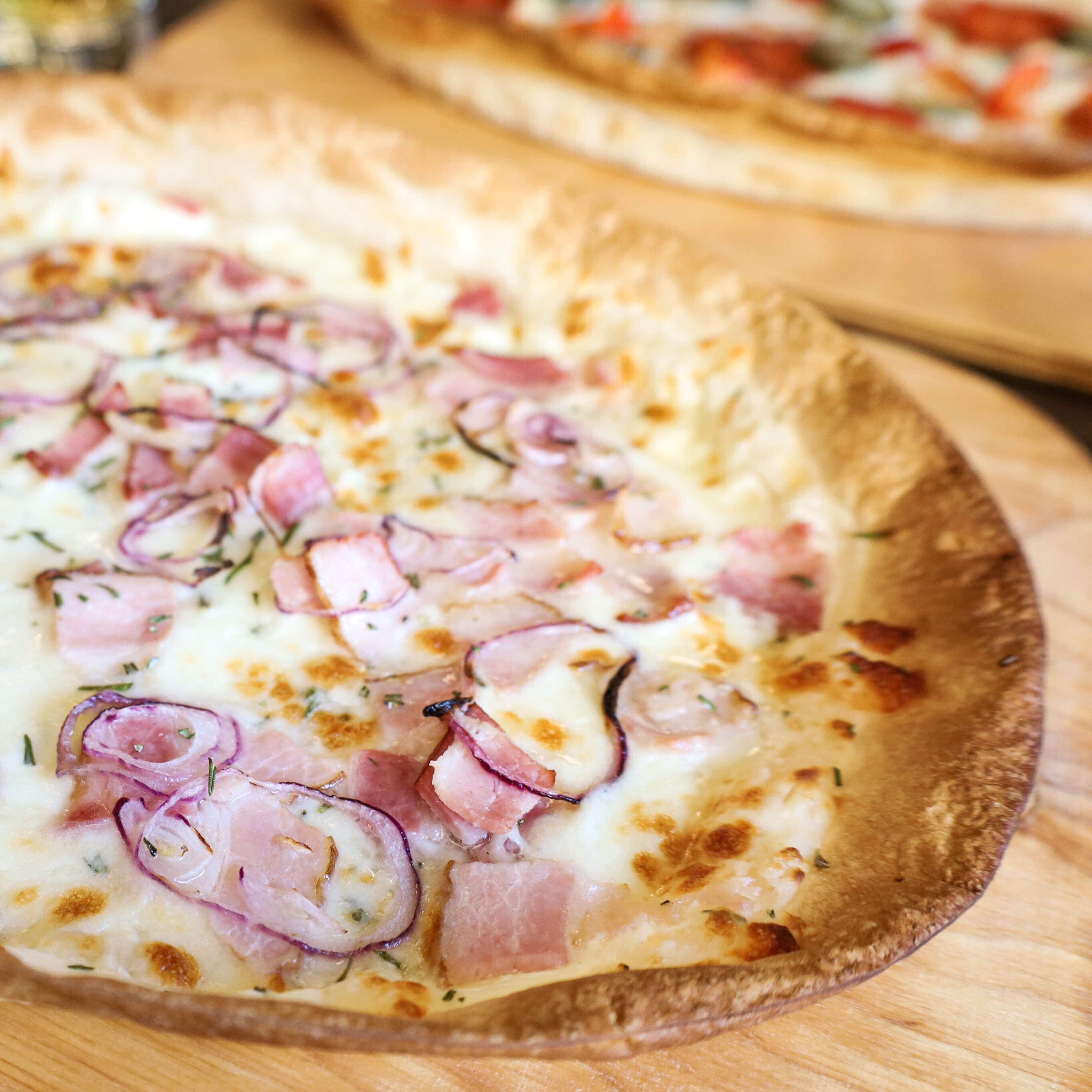 Pizza med skinke og løg på et træbræt.