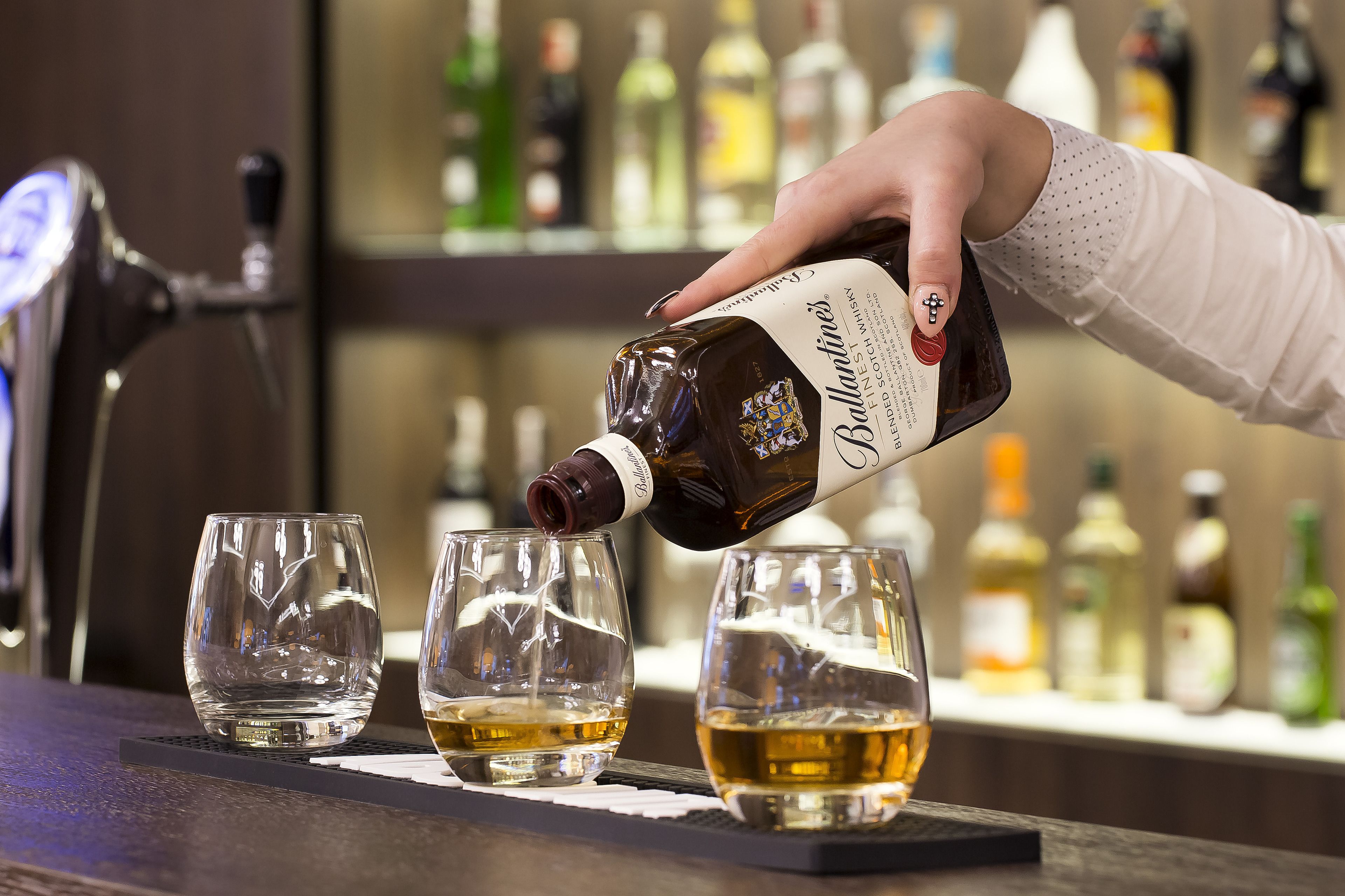 A hand pouring a dark liquid into three glasses on a bar counter.