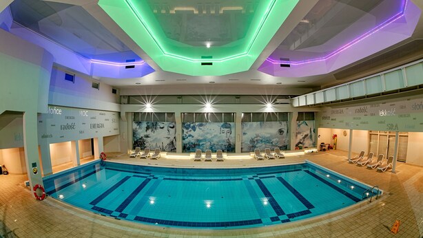 A large indoor swimming pool with multiple lanes, a central bar area, and lounge chairs around the pool.