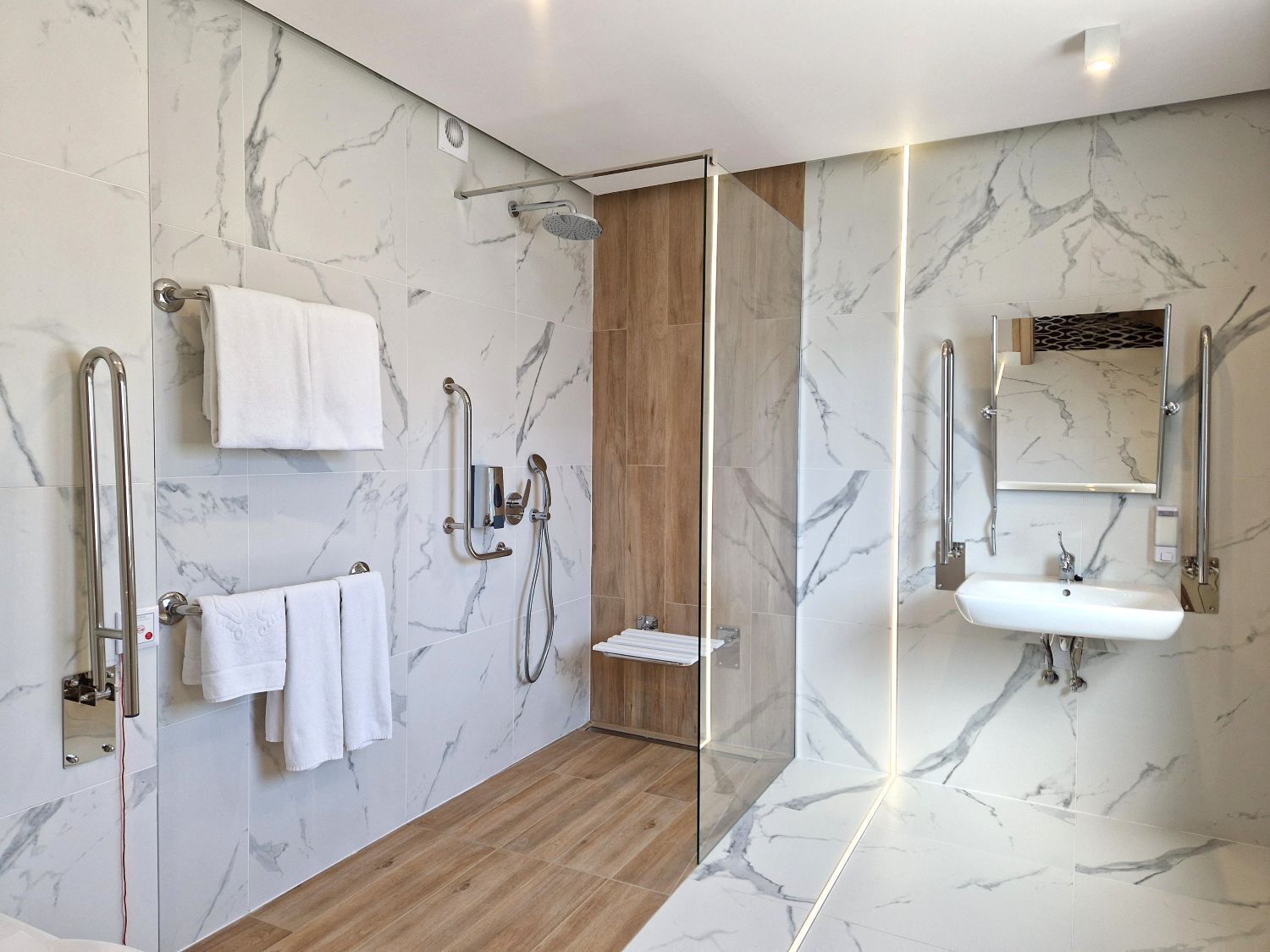 A modern bathroom with a glass-enclosed shower, marble walls, a wooden floor, a sink, and a mirror.