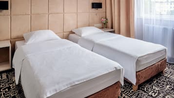 A hotel room with two beds, a TV mounted on the wall, a nightstand with a vase of flowers, and a window with curtains.