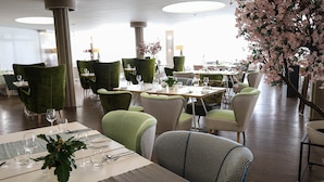 A restaurant with green upholstered chairs, white tables, and a large cherry blossom tree.