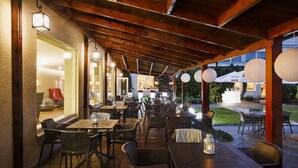 An outdoor dining area with wooden tables and chairs, lanterns, and a view of the garden.