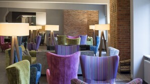 A lobby with colorful armchairs, a brick wall, and a modern ceiling design.
