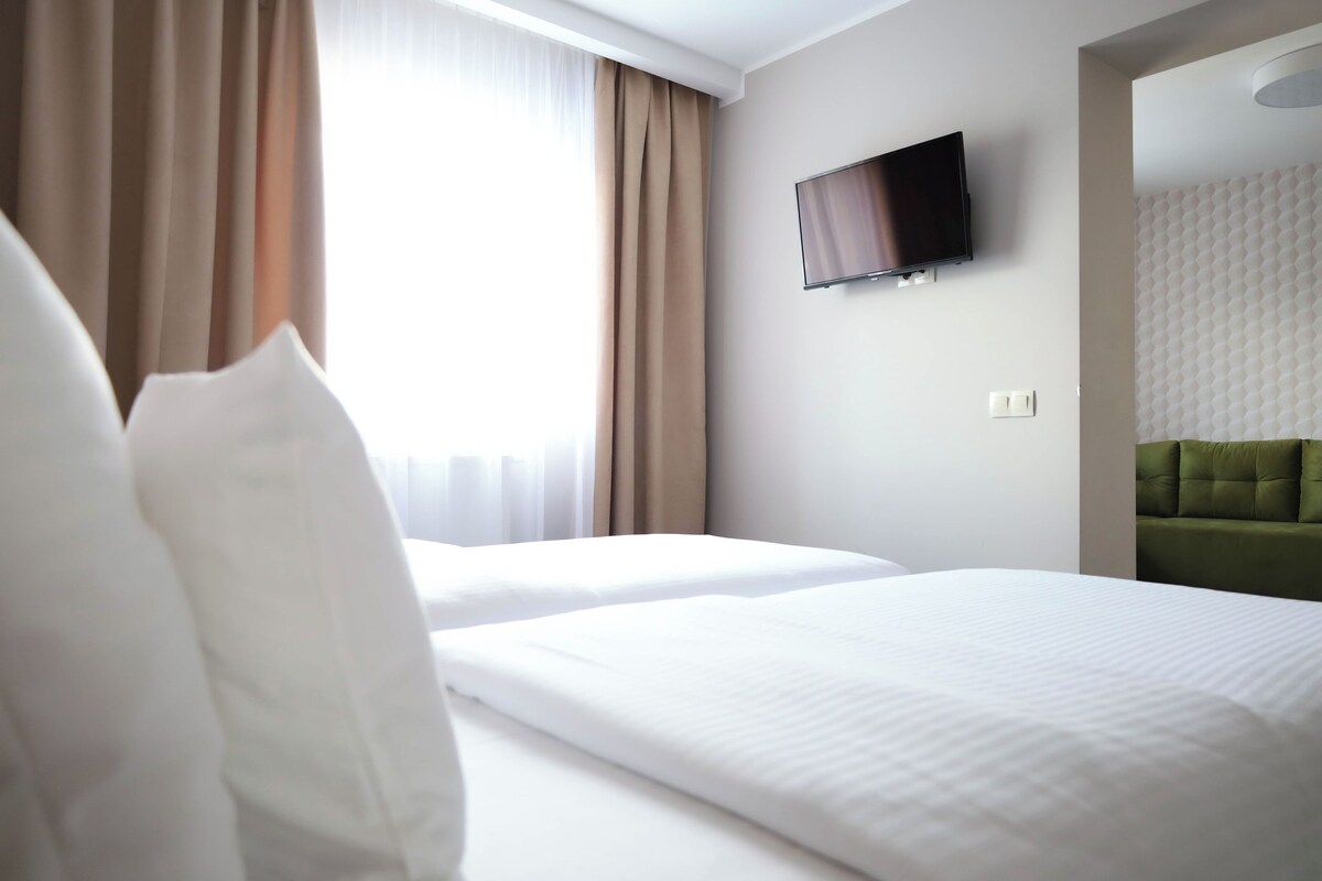 A hotel room with two beds, a flat-screen TV mounted on the wall, and a green upholstered headboard.