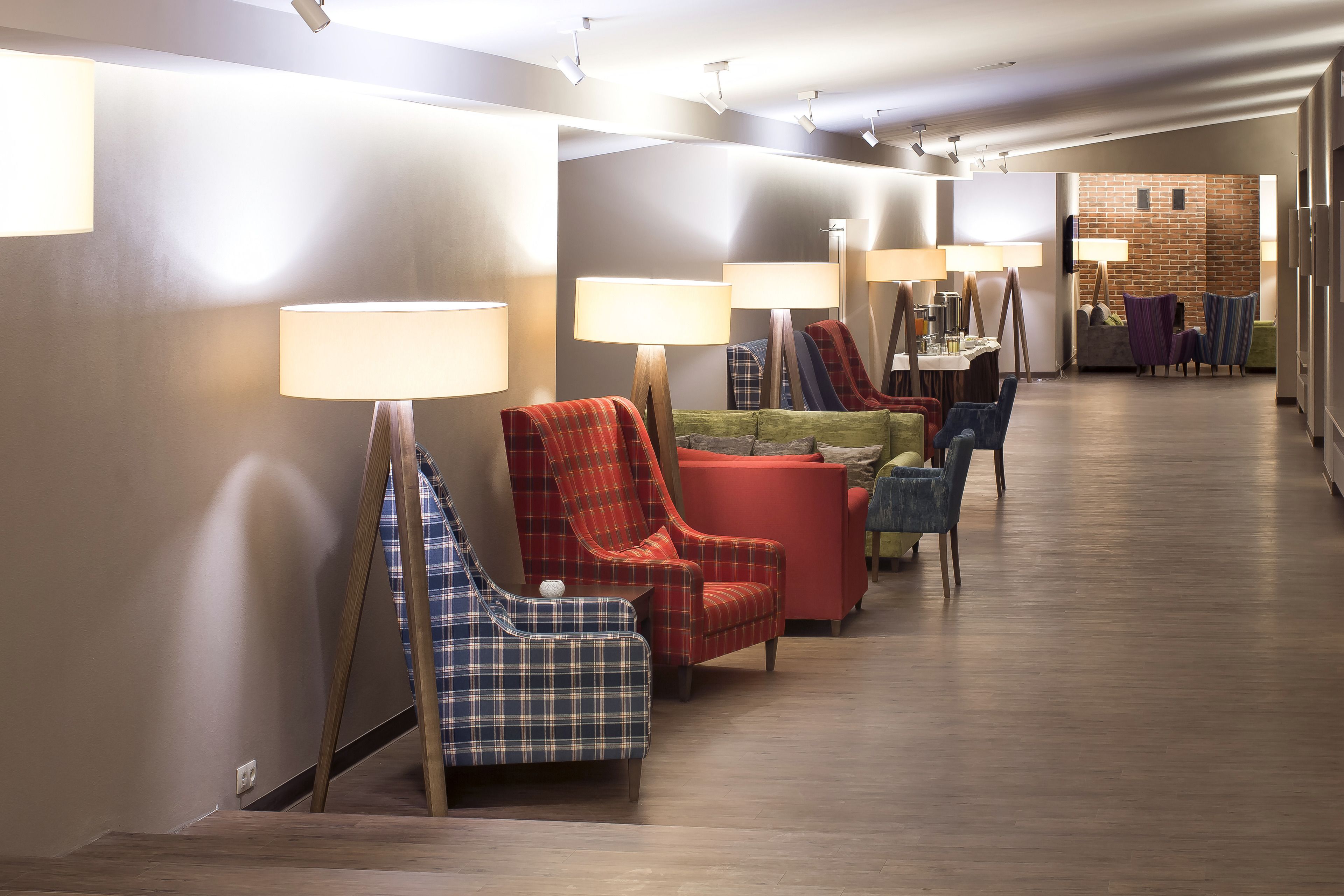 A hotel lobby with a row of armchairs and sofas, a reception desk, and a brick wall in the background.