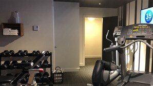Uma academia com equipamentos de cardio, halteres e uma TV exibindo '35 MILHÕES'.