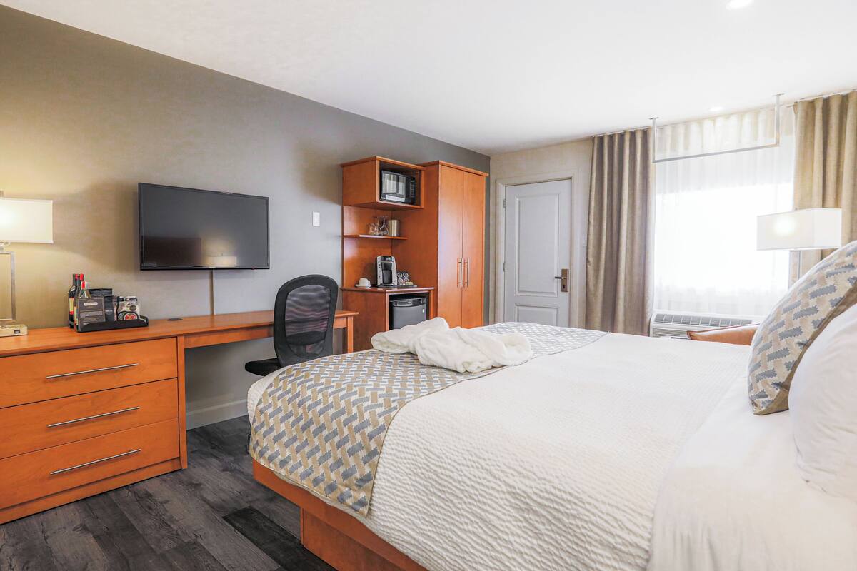 A hotel room with a bed, a desk with a television, a microwave, and a coffee maker.