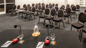 Sala de conferências com fileiras de cadeiras e mesas, equipada com microfones e copos de água.