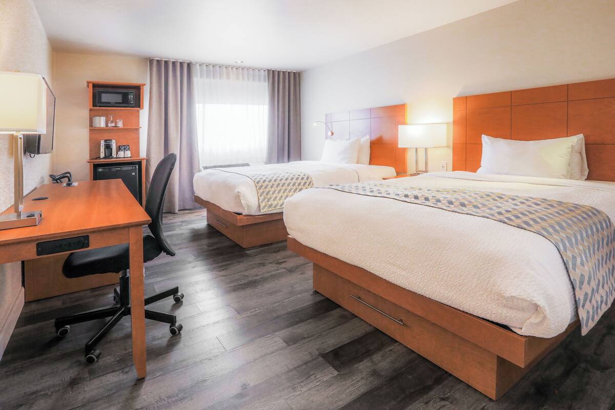 A hotel room with two beds, a desk with a chair, a microwave, and a coffee maker.