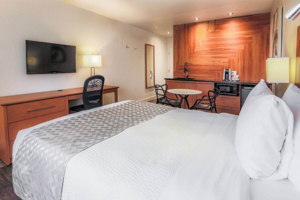 A hotel room with a bed, a desk, a chair, a television, a microwave, and a small kitchenette.