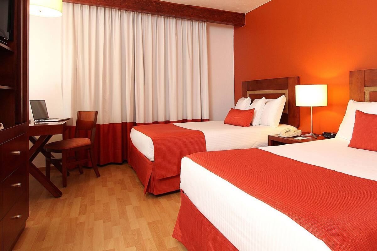 A hotel room with two beds, a desk, a chair, a lamp, and a telephone.