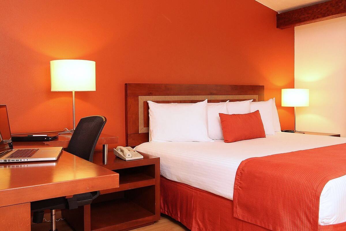 A hotel room with a bed, desk, chair, and two bedside lamps.