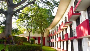 Ein Gebäude mit roter und weißer Fassade, mehreren Balkonen und einem gepflegten Garten mit verschiedenen Pflanzen.