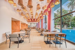 A spacious indoor dining area with multiple tables and chairs, large windows with a view of palm trees and a pool, and hanging wicker lamps. - Fiesta Inn Villahermosa Cencali (Villahermosa)