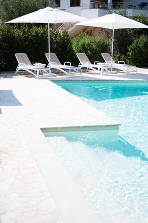 A pool area with white lounge chairs and umbrellas, surrounded by greenery.