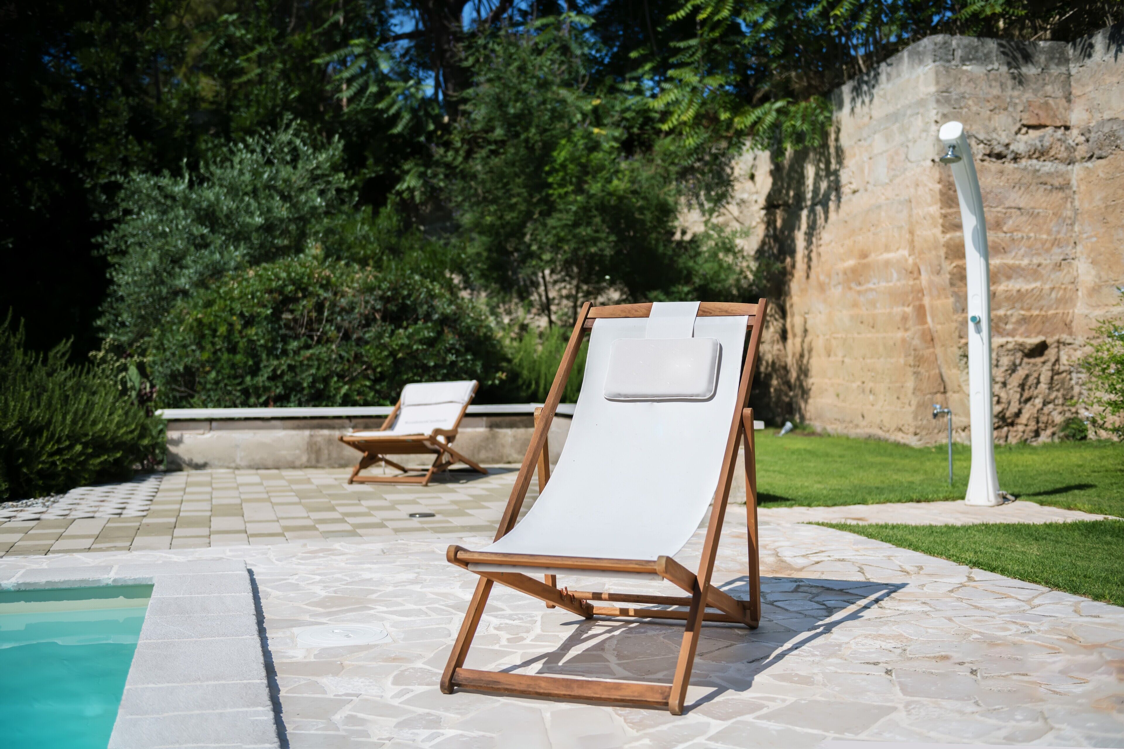 A poolside area with two wooden lounge chairs and a stone-tiled deck.