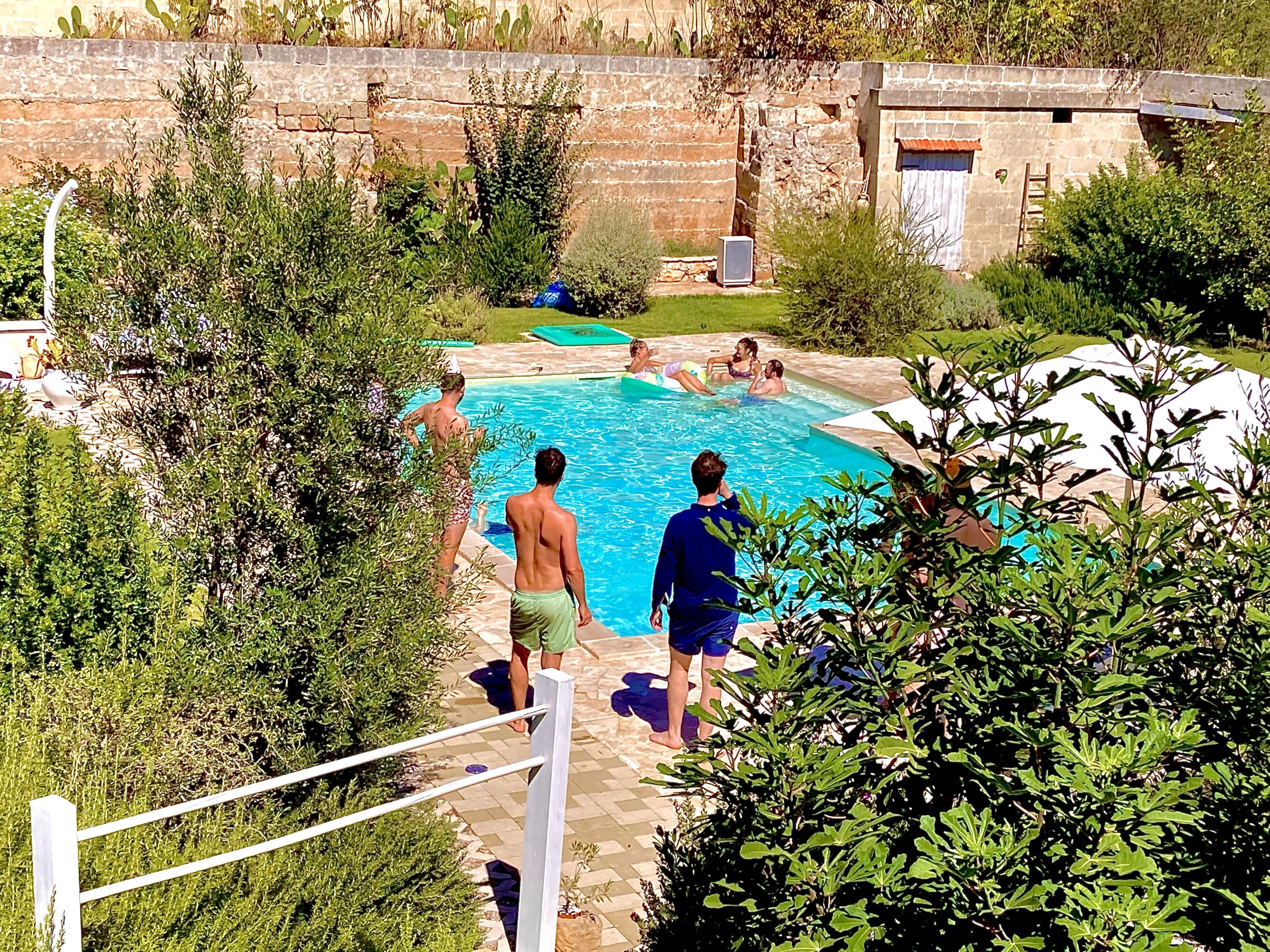 Ein Pool, umgeben von viel Grün, mit einer Steinmauer und einem kleinen Gebäude im Hintergrund.