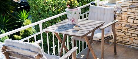 An outdoor patio with a wooden table and two cushioned chairs, surrounded by a white railing and stone wall.