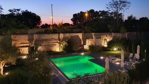Una piscina con muro de piedra y sillones de descanso.