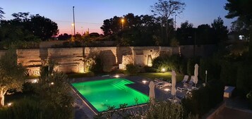 Una piscina con muro de piedra y sillones de descanso.