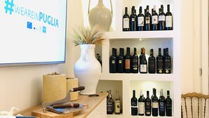 Una bodega con estantes llenos de botellas de vino, un televisor mostrando #WEAREINPUGLIA y un jarrón decorativo.