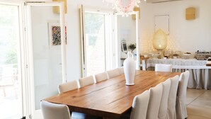 Un comedor amplio con una mesa de madera y sillas blancas, una lámpara decorativa y vistas al exterior a través de puertas de cristal grandes.