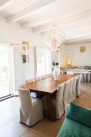 Un comedor amplio con una mesa de madera y sillas blancas, una lámpara decorativa y vistas al exterior a través de puertas de cristal grandes.